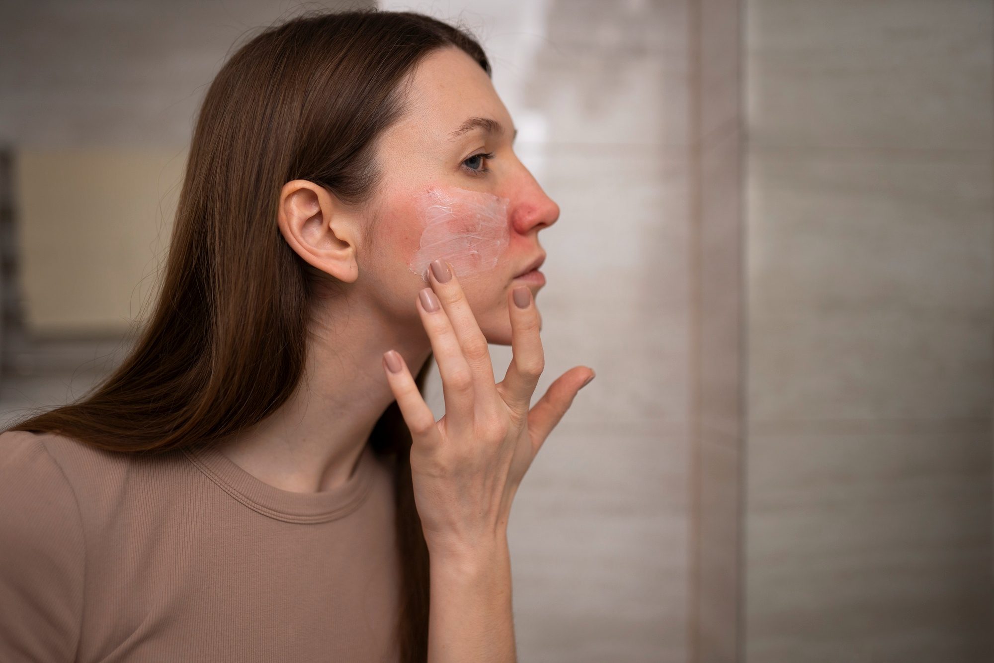 Woman examining her facial skin closely in a mirror.