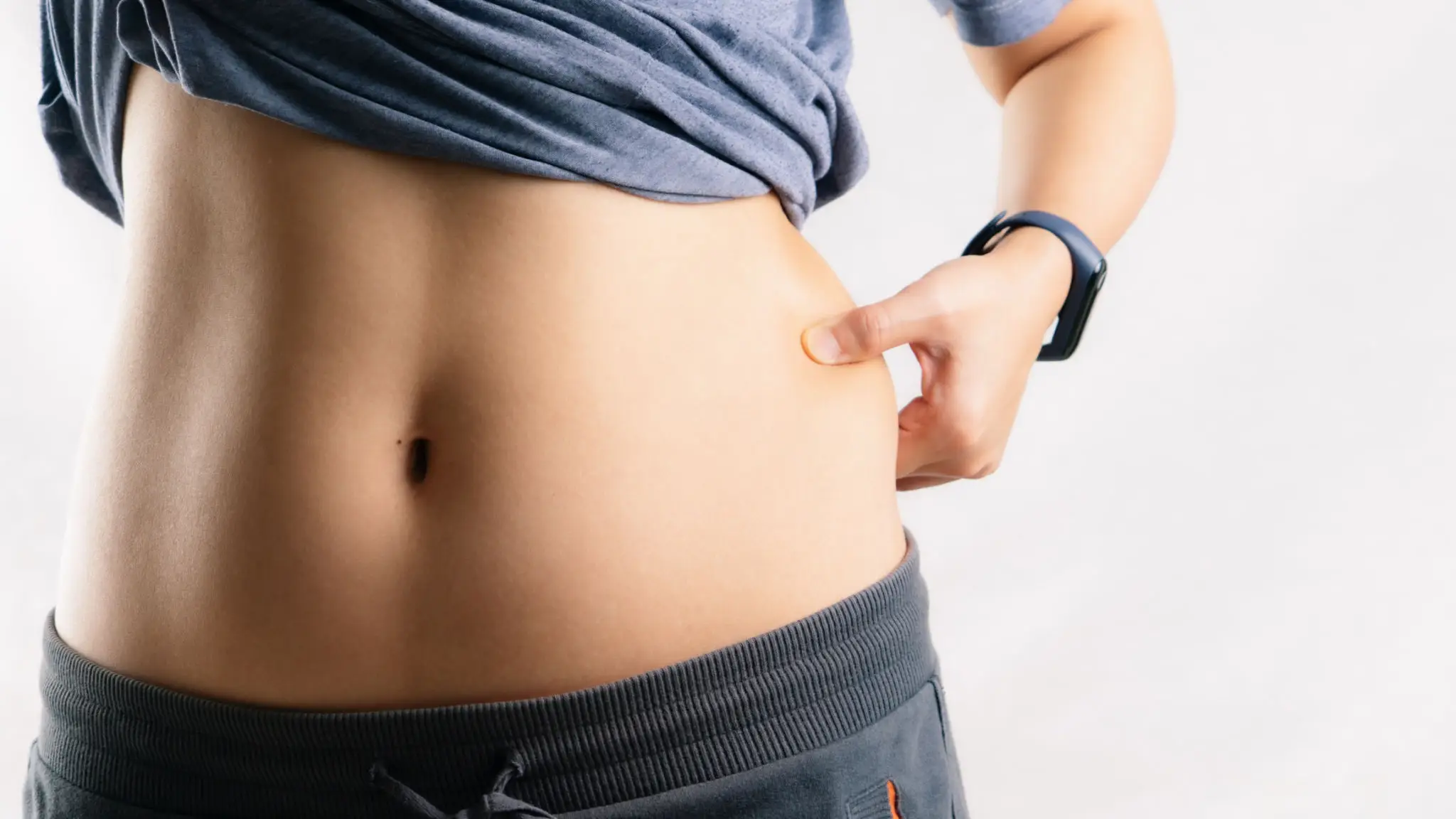 Person pinching belly fat near waistline in casual clothes.