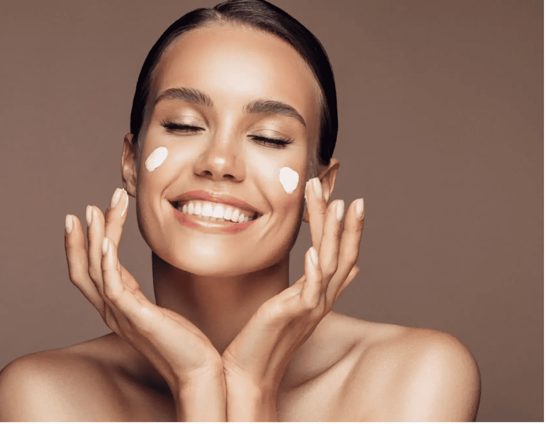 Woman applying moisturizer on her face with a joyful expression.