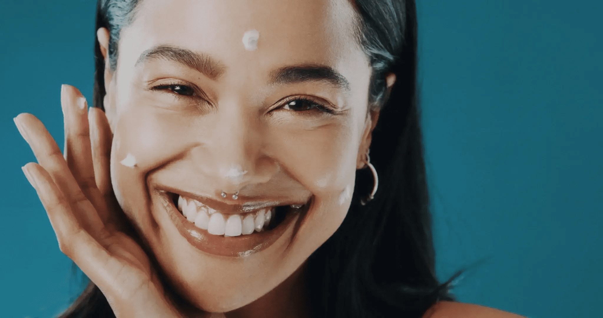 Close-up of a smiling woman with a nose ring and earrings.