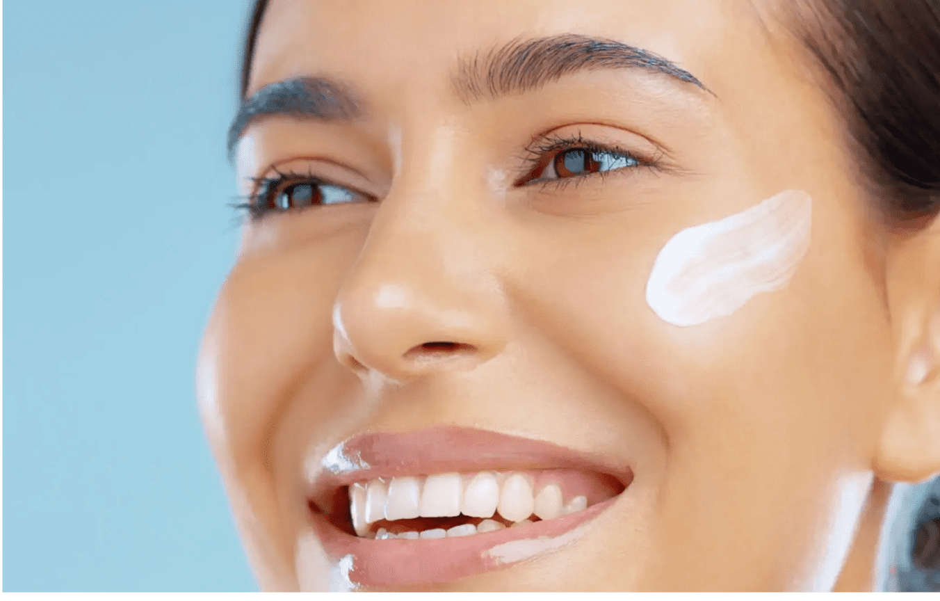 Smiling woman applying cream to her cheek.