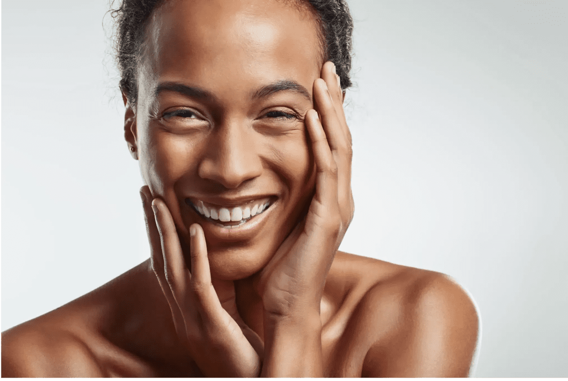 Close-up of a smiling person with hands gently touching their face.