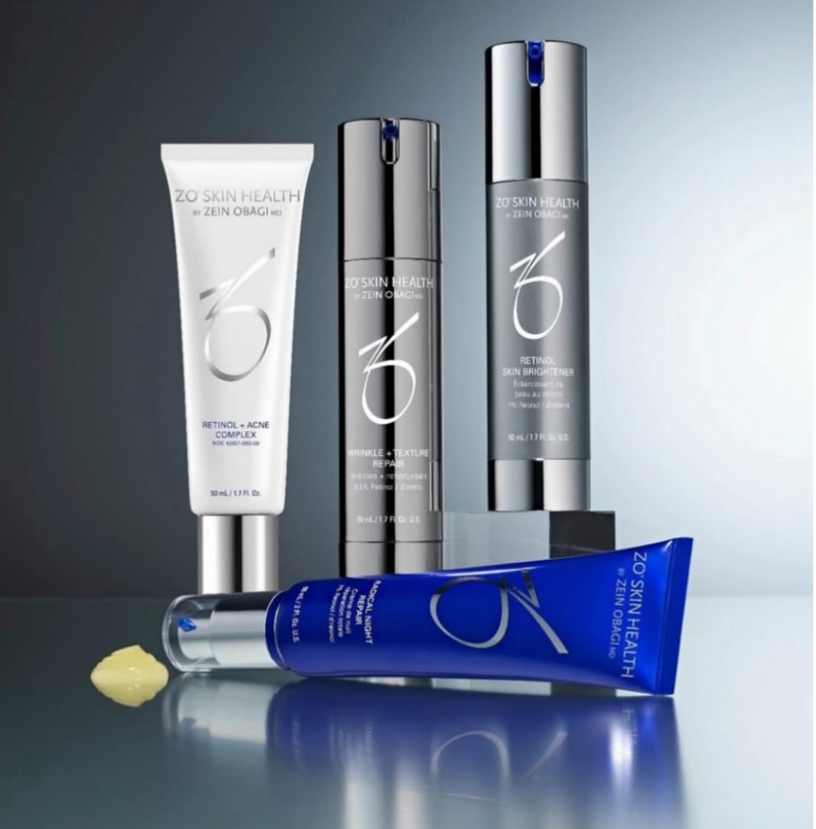 Four sleek skincare products arranged with reflective surface and soft lighting.