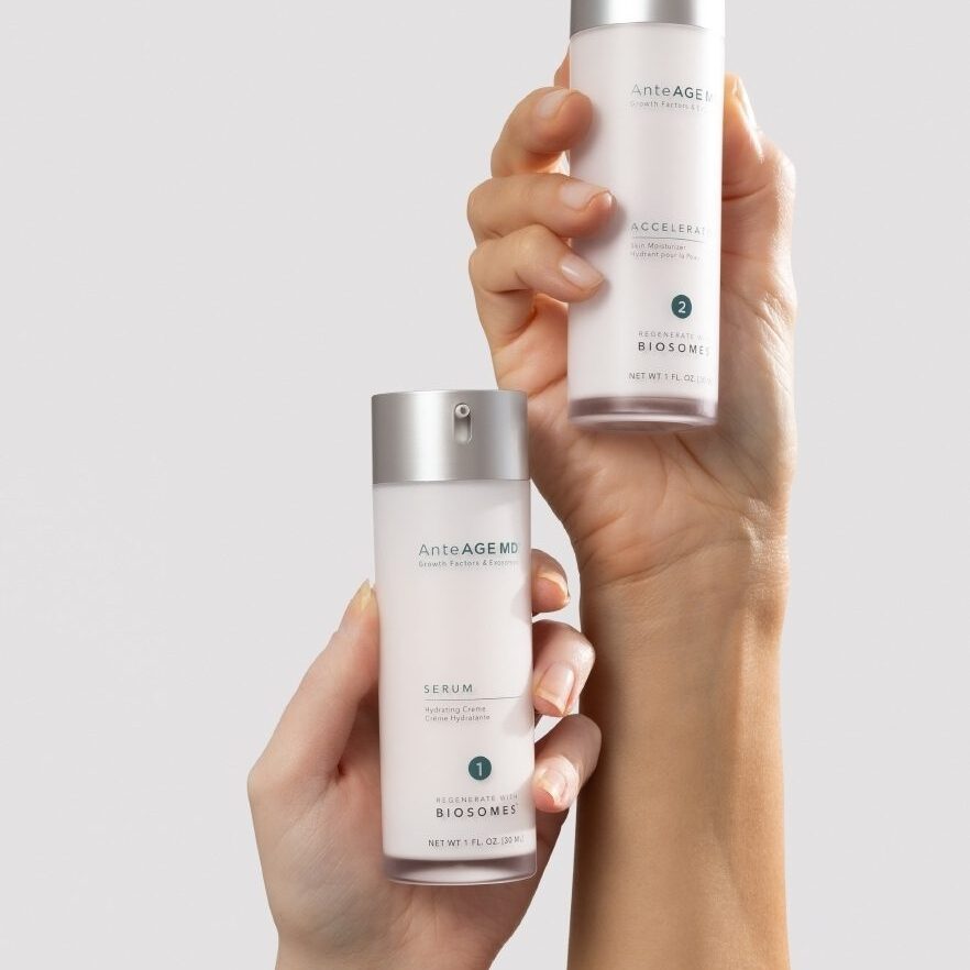 Two hands holding white skincare bottles with silver caps.