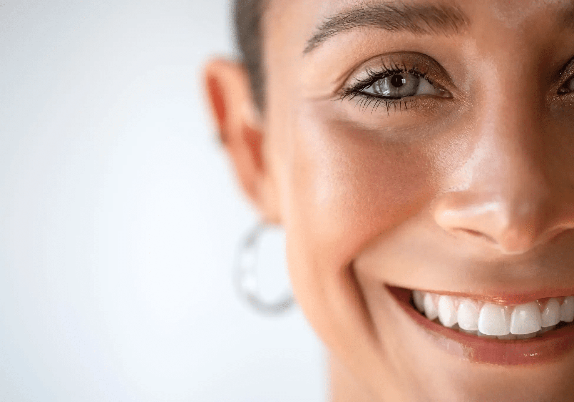 Close-up of a smiling woman with hoop earrings and clear skin.
